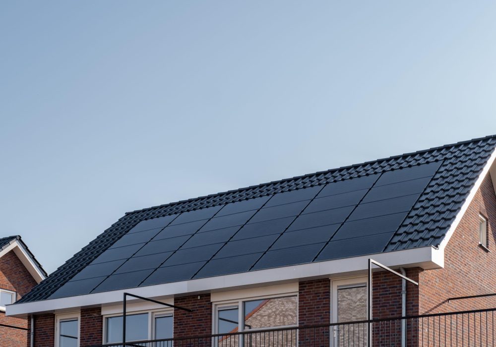 Newly build houses with solar panels attached on the roof against a sunny sky Close up of new building with black solar panels. Zonnepanelen, Zonne energie, Translation: Solar panel, , Sun Energy. Netherlands